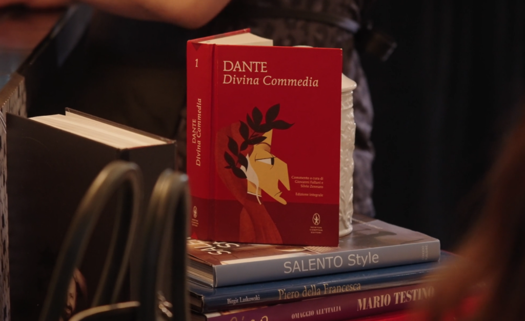 The best italian restaurant in houston. Image of a stack of books. A red one is vertical on top, it is a red cover with a face on it, titled, Dante Divina Commedia